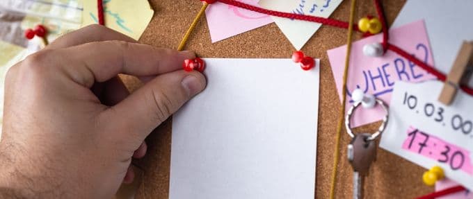 A cork board full of clues connected by red string.