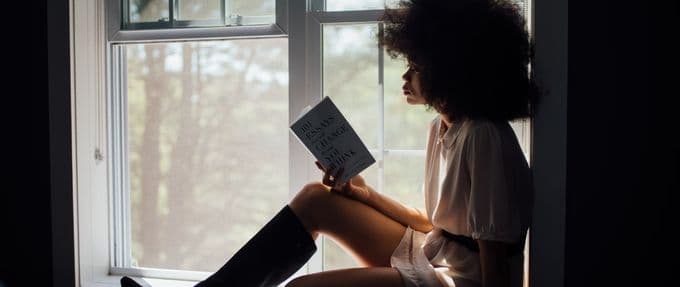 A woman sits in the window reading a book.