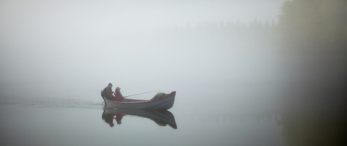two people fishing in a canoe on an eerie, cloudy lake