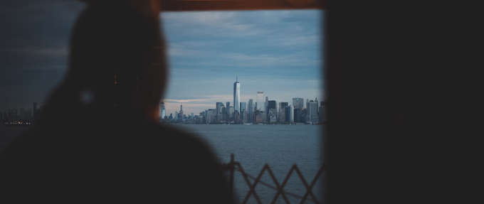 girl looking out a window at nyc skyline beyond the water